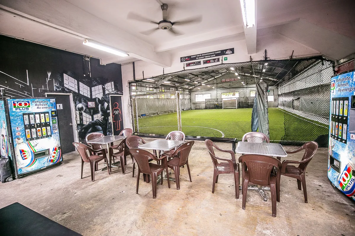 Tables and chairs beside a netted playing arena at The Cage @ Kallang